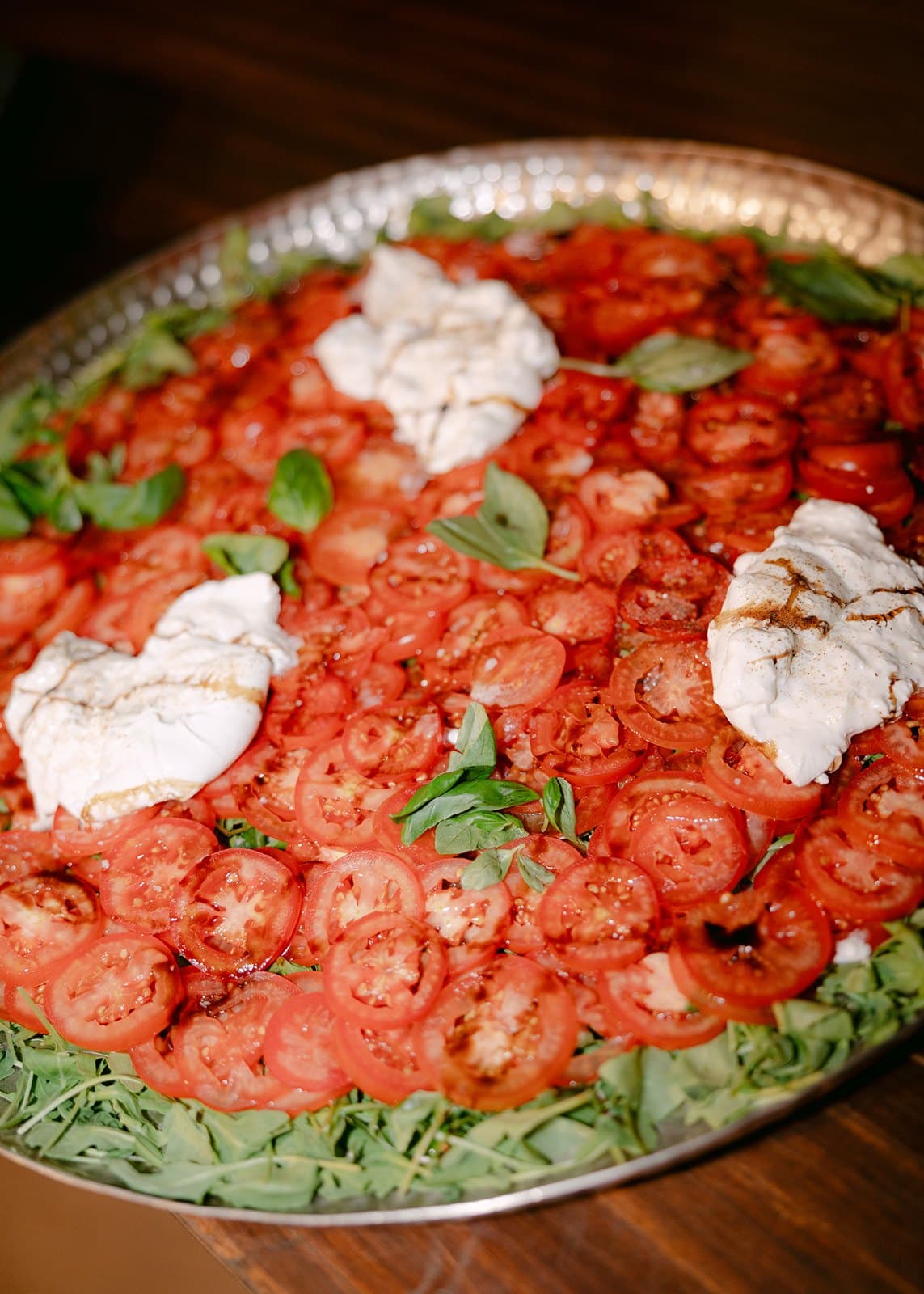 Tomate às rodelas com burrata, manjericão e rúcula, numa travessa para partilhar.