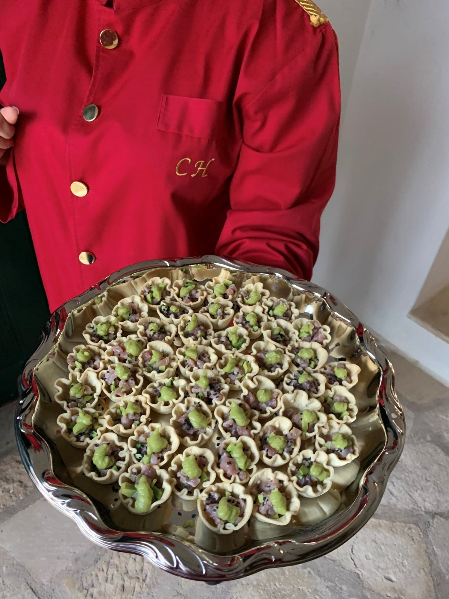 Equipa Carlota C.H., de farda vermelha com o monograma CH, a servir uma bandeja de canapés